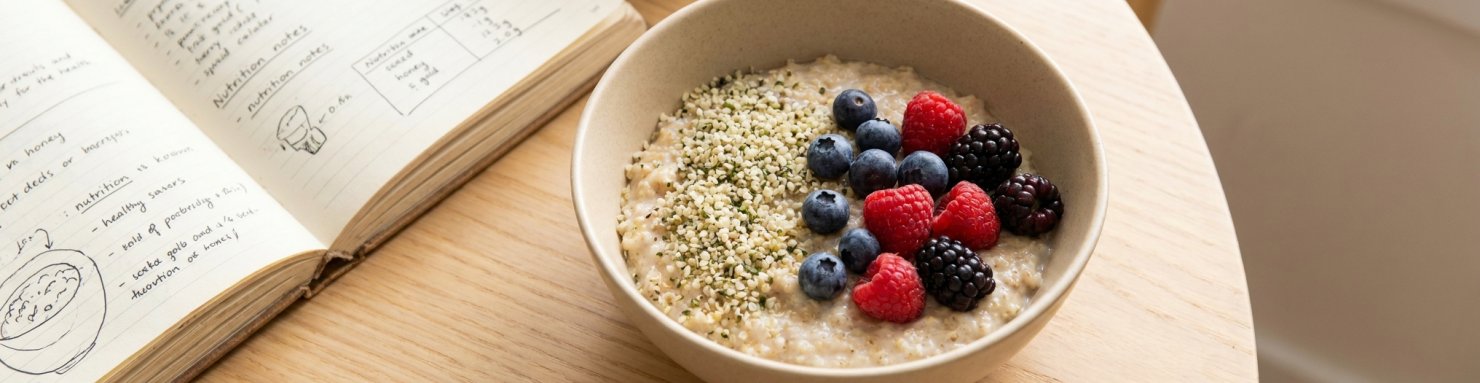 Bol de porridge garni de graines de chanvre et de baies fraîches accompagné d'un carnet de nutrition pour choisir entre chanvre, lin et chia selon son objectif