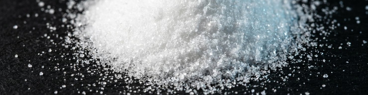 Cristaux blancs purs d'isolat de CBD à 99 % sur fond noir mat illustrant la pureté du cannabidiol